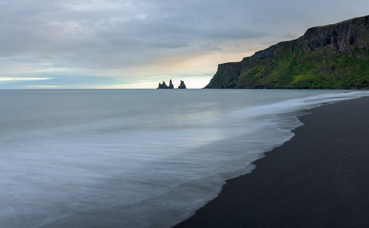 Die Bucht von Vík í Mýrdal im Süden Islands im Licht eines Abends im Juni. Im Hintergrund ragen die Basaltfelsen Reynisdrangar, das Wahrzeichen des Ortes, aus dem Meer empor.