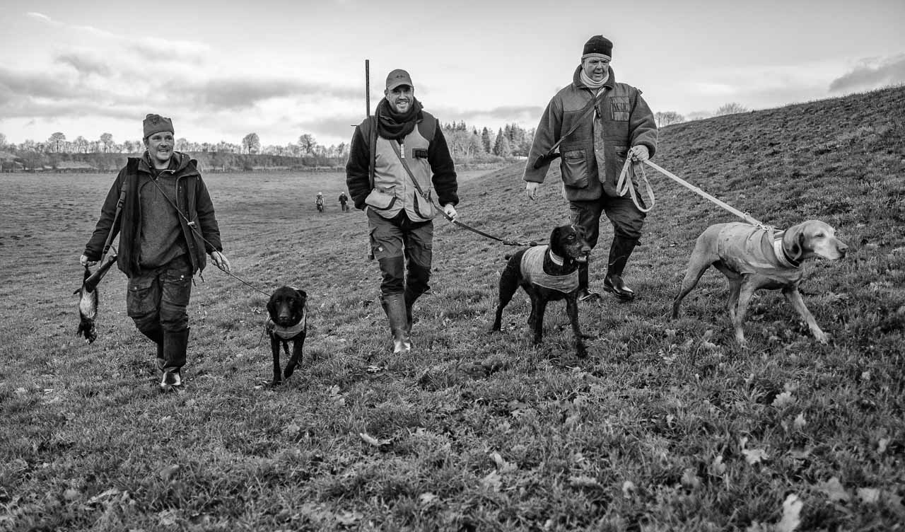 Szenen einer Jagd: Bei einer Bewegungsjagd werden etliche Kilometer zurückgelegt. Die Aufnahme der drei Jäger mit ihren Hunden entstand in Schleswig-Holstein im Dezember 2018.